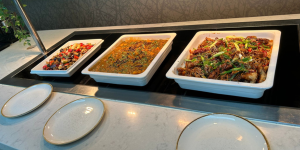 Multiple serving plates of professionally prepared hot buffet foods, including roast vegetables, ready for event attendees to serve themselves.