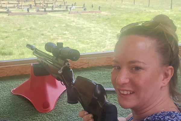a person smiles while holding a rifle at a shooting range